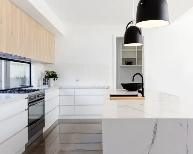 Modern kitchen featuring sleek white cabinetry, a marble countertop, black pendant lights, and a large window for natural light